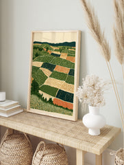 Stylised landscape art print showing geometric farm fields, rolling hills, and trees in, in an alternate framed mockup