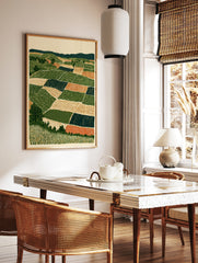 Stylised landscape art print showing geometric farm fields, rolling hills, and trees in green, tan, in a styled room mockup