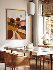 Minimalist landscape art print with rolling hills, three stylized trees, and a sun in earthy tones, in a styled room mockup