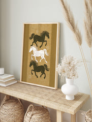 Three stylised running horses, two dark and one white, on an earthy golden-brown background, in an alternate framed mockup