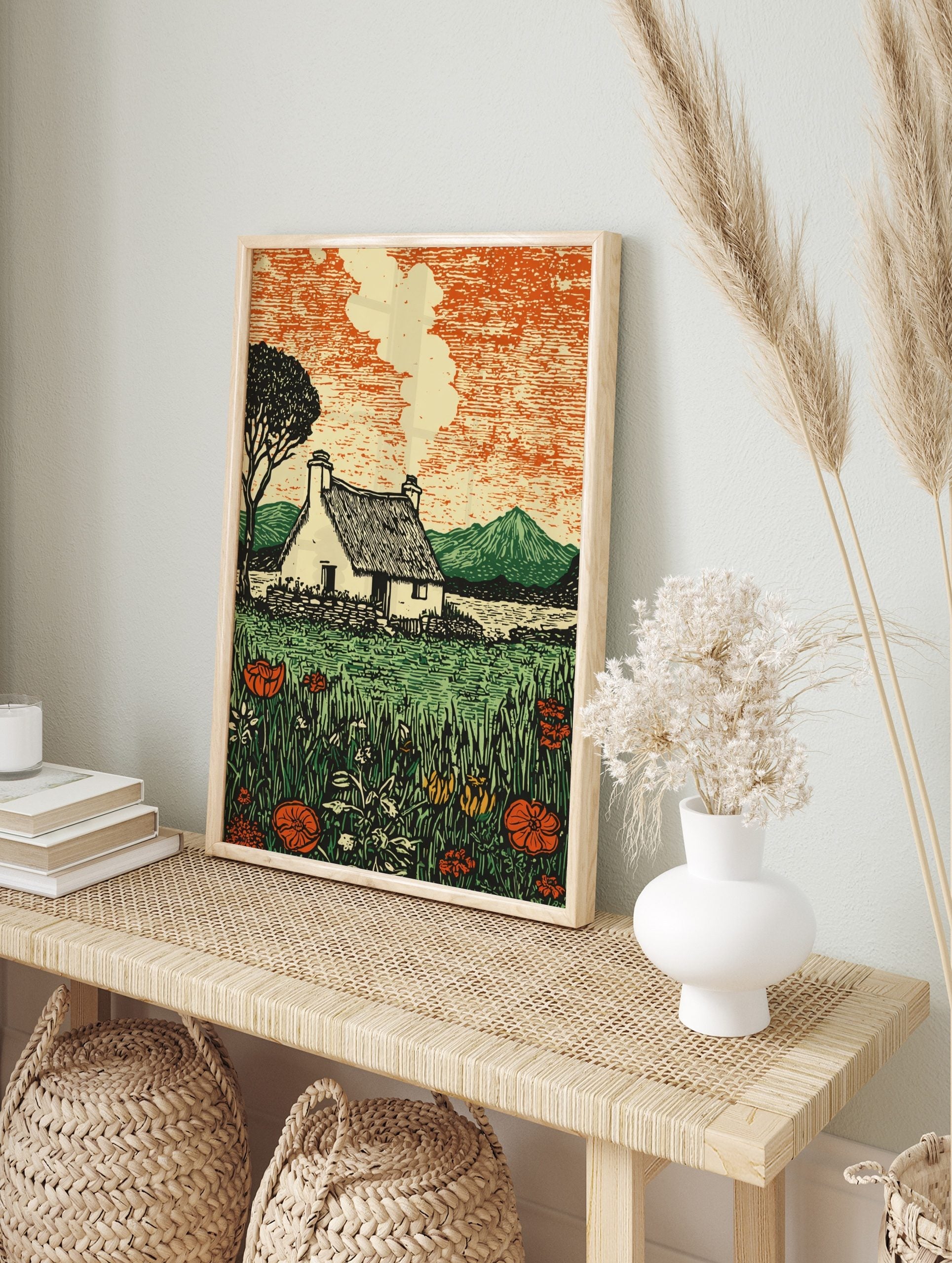 Illustrative print of a rural cottage with thatched roof, smoke, lake, mountains, and, in an alternate framed mockup