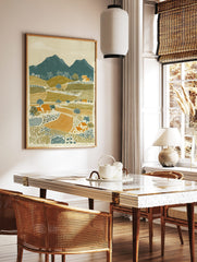 Illustrative rural landscape print with teal mountains, olive green hills, orange fields, and small, in a styled room mockup