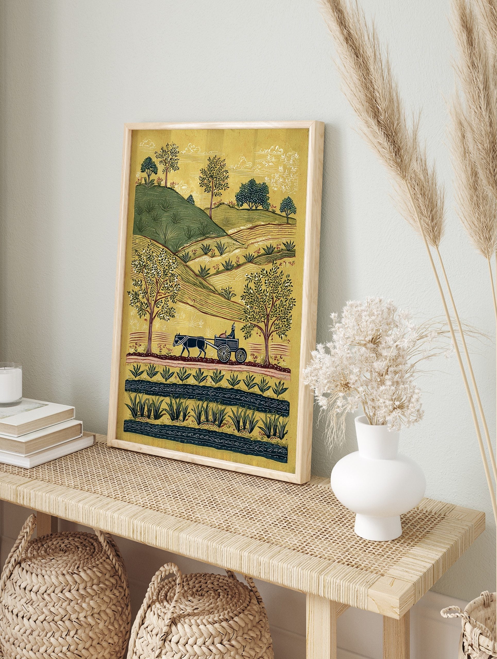 Folk art rural landscape print with an ox-drawn cart, green hills, trees, and a stream on a, in an alternate framed mockup