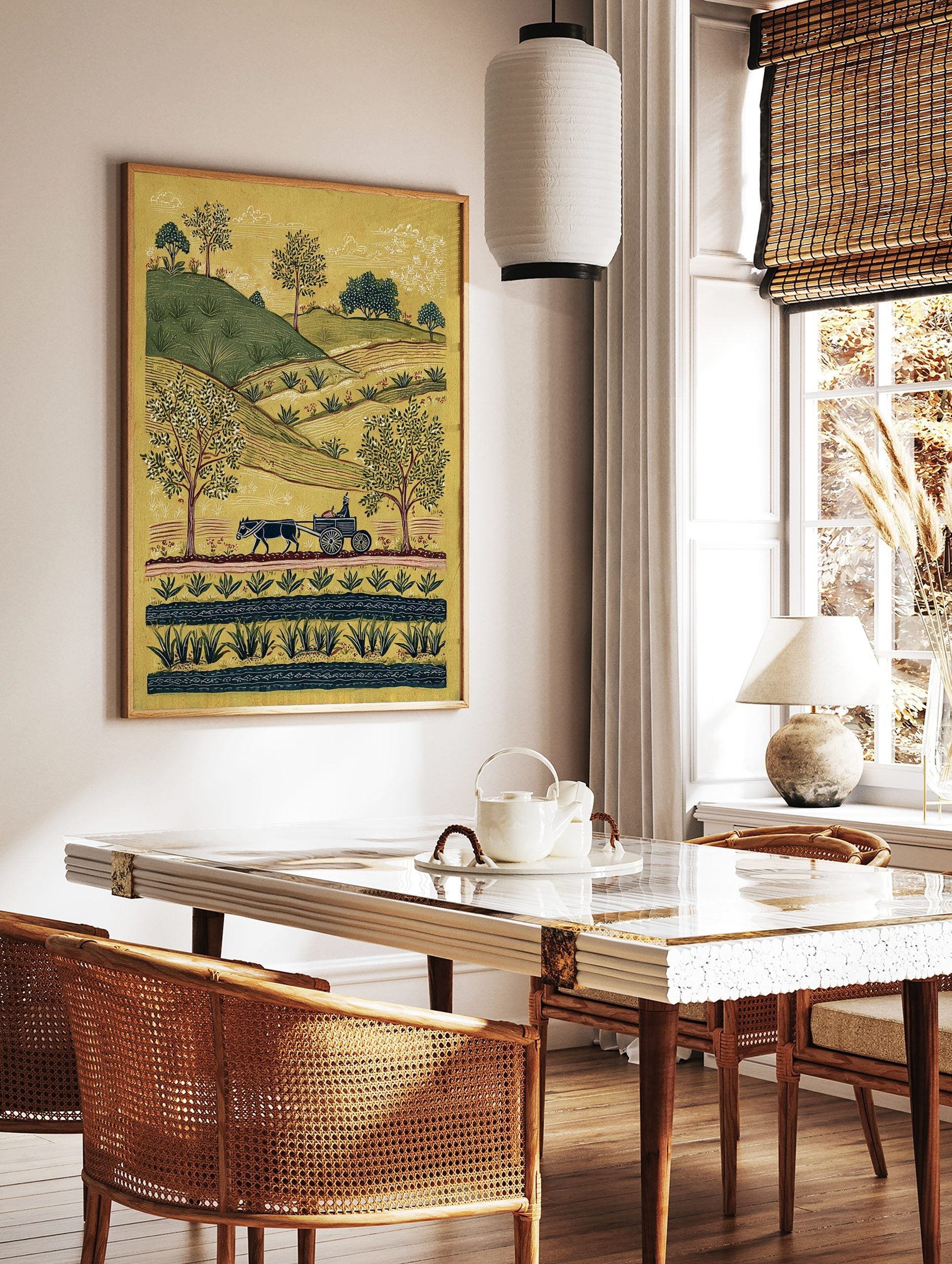 Folk art rural landscape print with an ox-drawn cart, green hills, trees, and a stream on a yellow, in a styled room mockup