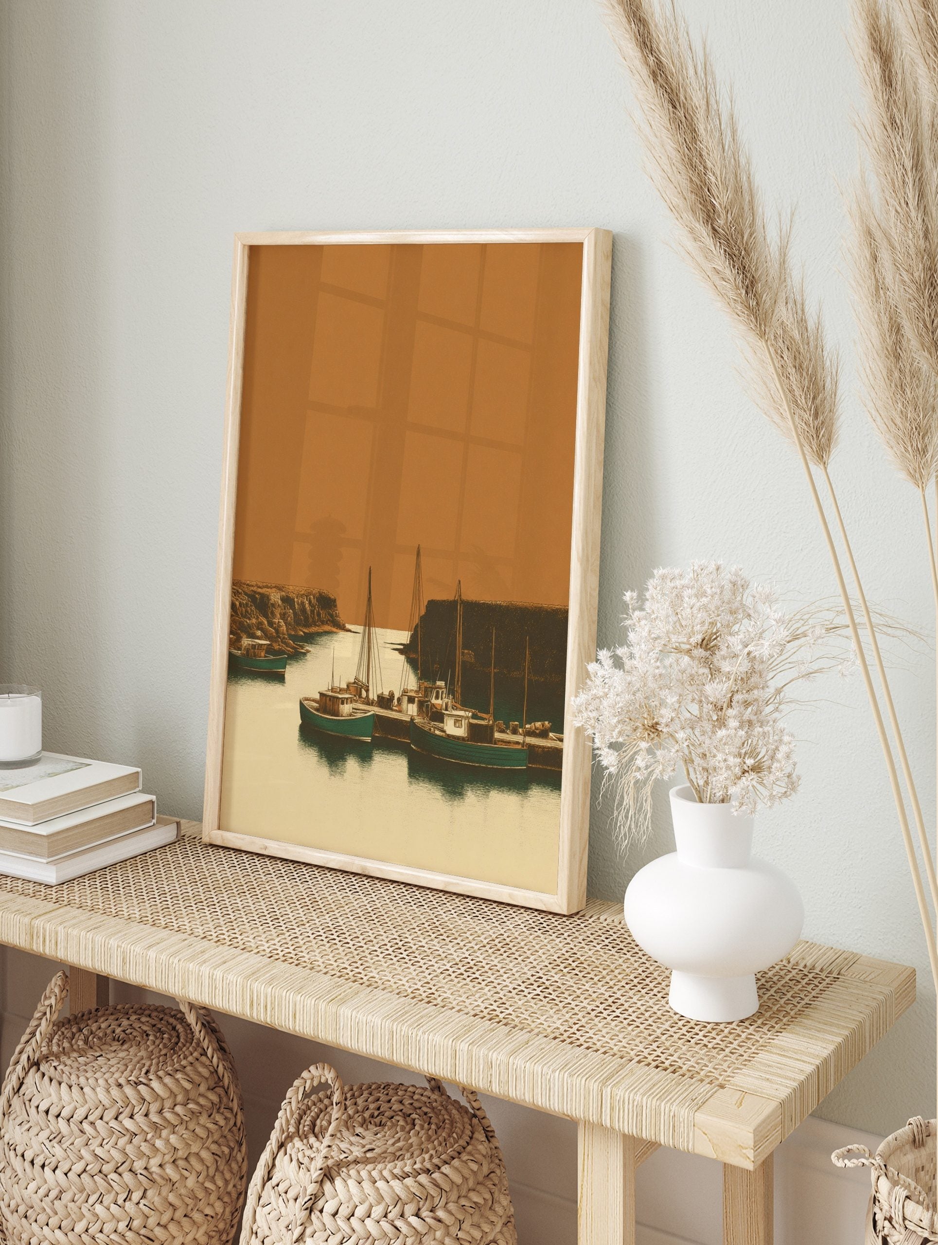 Illustrative print of fishing boats in a rustic harbour, flanked by rocky cliffs under an, in an alternate framed mockup
