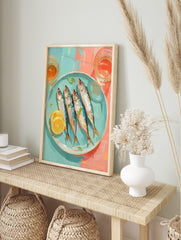 Illustrative wall art of four whole sardines with lemon and herbs on a blue plate, with, in an alternate framed mockup