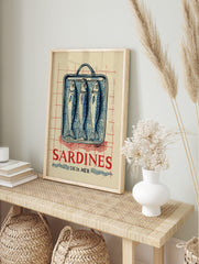 Vintage-style illustration of three blue sardines in a tin can with red 'SARDINES DE LA MÈR', in an alternate framed mockup