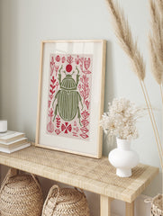 Olive green scarab beetle print with white stripes, surrounded by red abstract botanical, in an alternate framed mockup