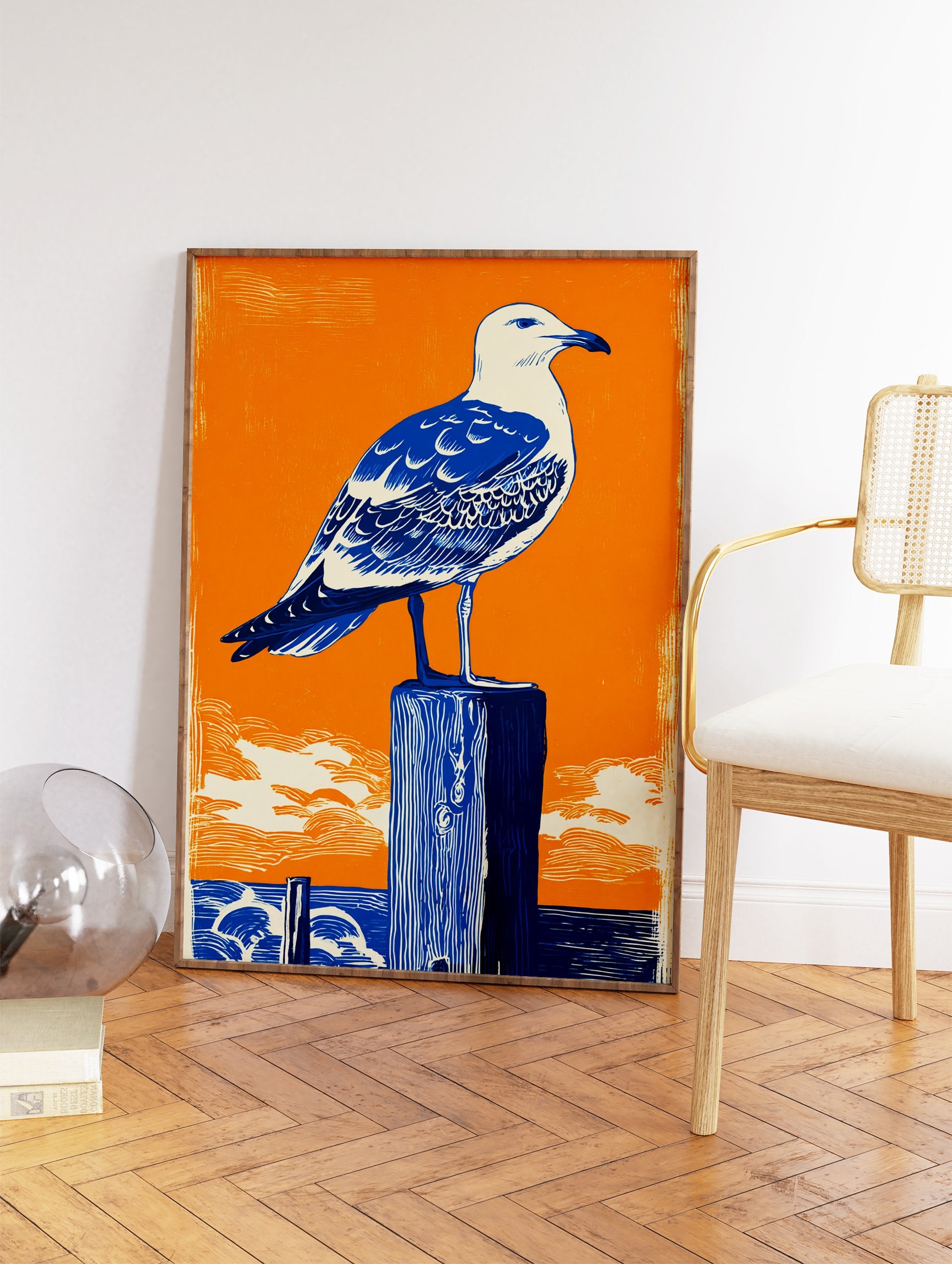 Seagull Wall Art linocut print featuring a blue and white seagull on a dark blue wooden post against an orange sky and ocean. - Image 2