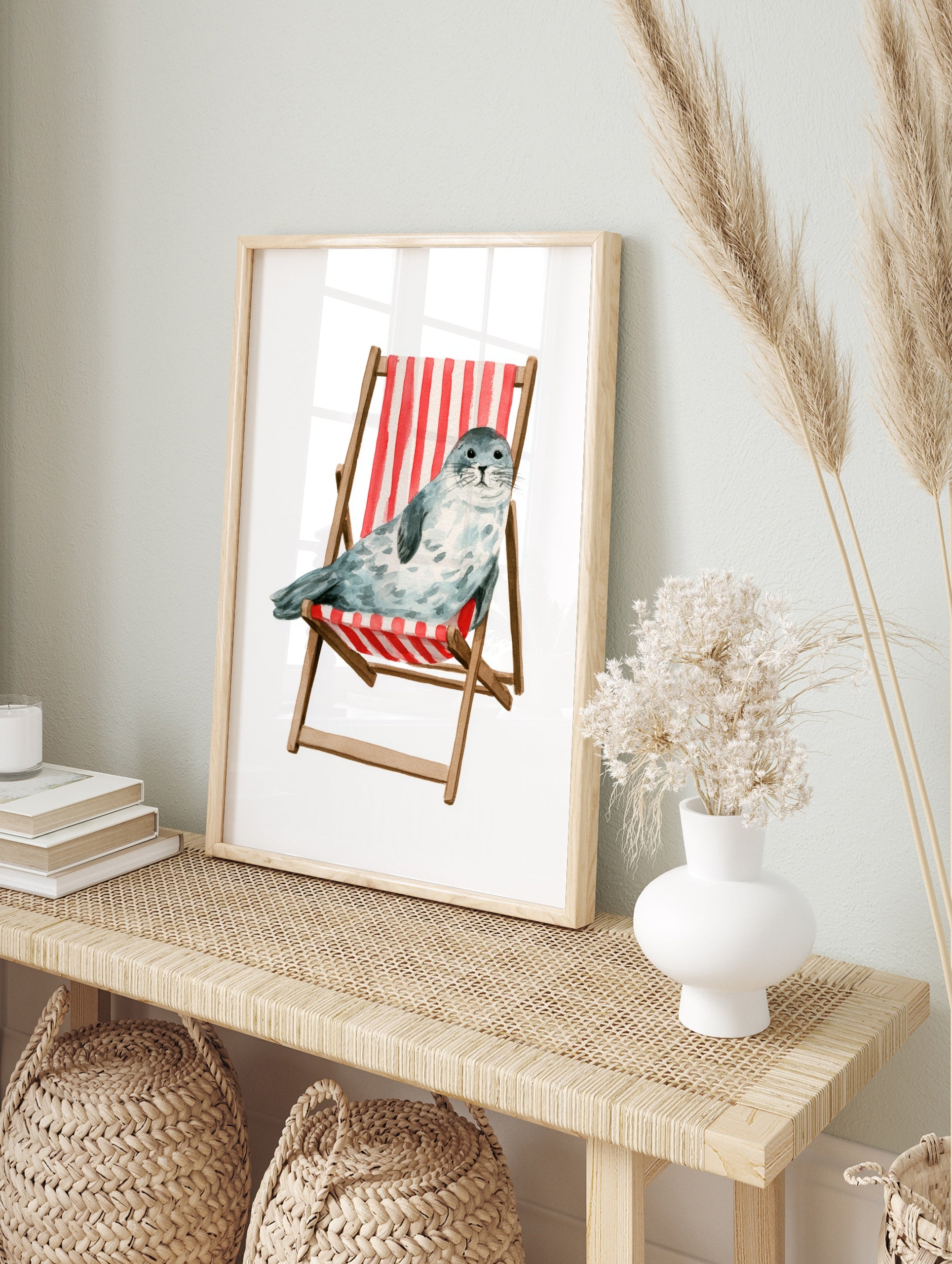Watercolour illustration of a spotted grey seal sitting in a red and white striped wooden, in an alternate framed mockup