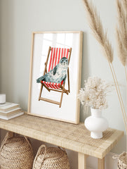 Watercolour illustration of a spotted grey seal sitting in a red and white striped wooden, in an alternate framed mockup