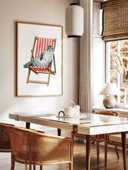 Watercolour illustration of a spotted grey seal sitting in a red and white striped wooden deckchair, in a styled room mockup