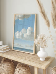 Seascape painting with blue sky, white cumulus clouds, calm ocean, and two small distant, in an alternate framed mockup