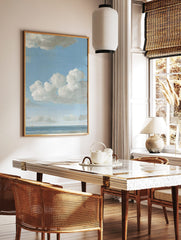 Seascape painting with blue sky, white cumulus clouds, calm ocean, and two small distant boats on, in a styled room mockup