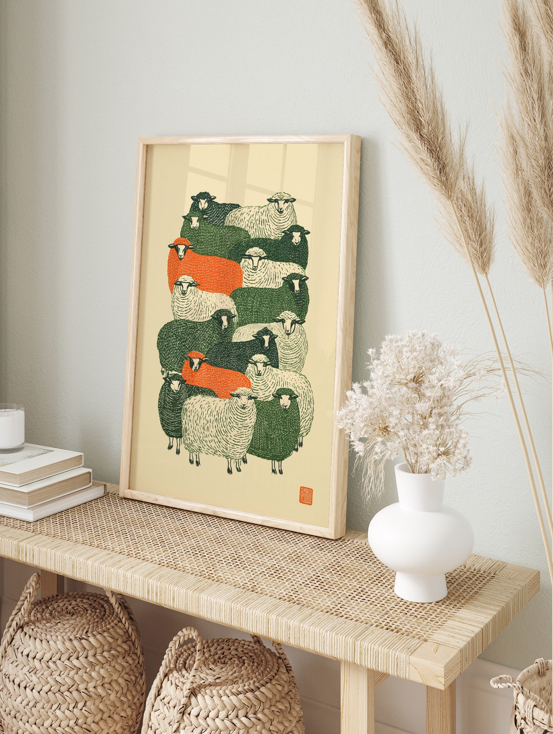 Stylised flock of sheep in green, orange, and cream colours, graphic linocut-inspired art, in an alternate framed mockup