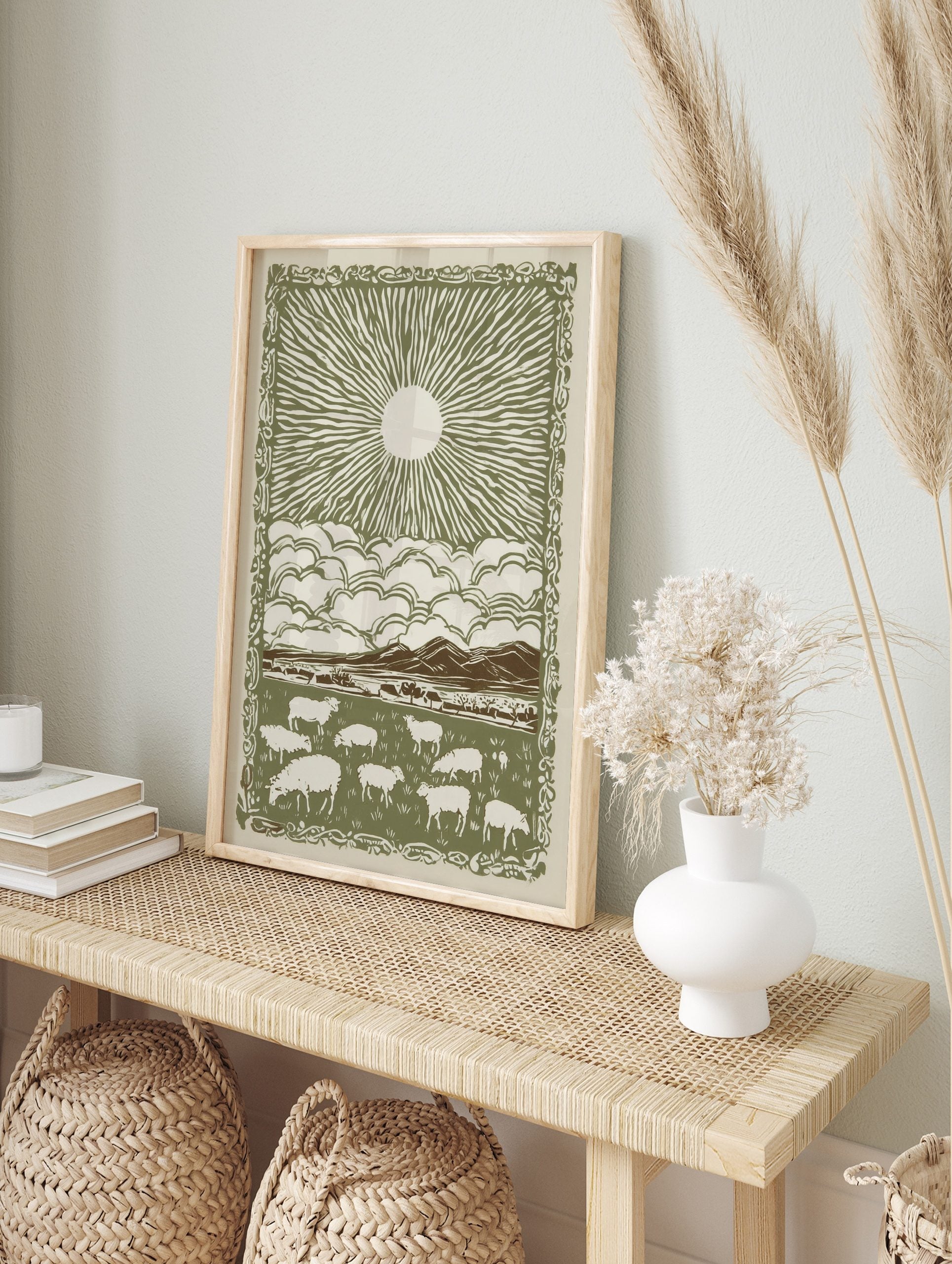 Illustrative green and off-white print of sheep grazing in a field beneath a sun and clouds, in an alternate framed mockup
