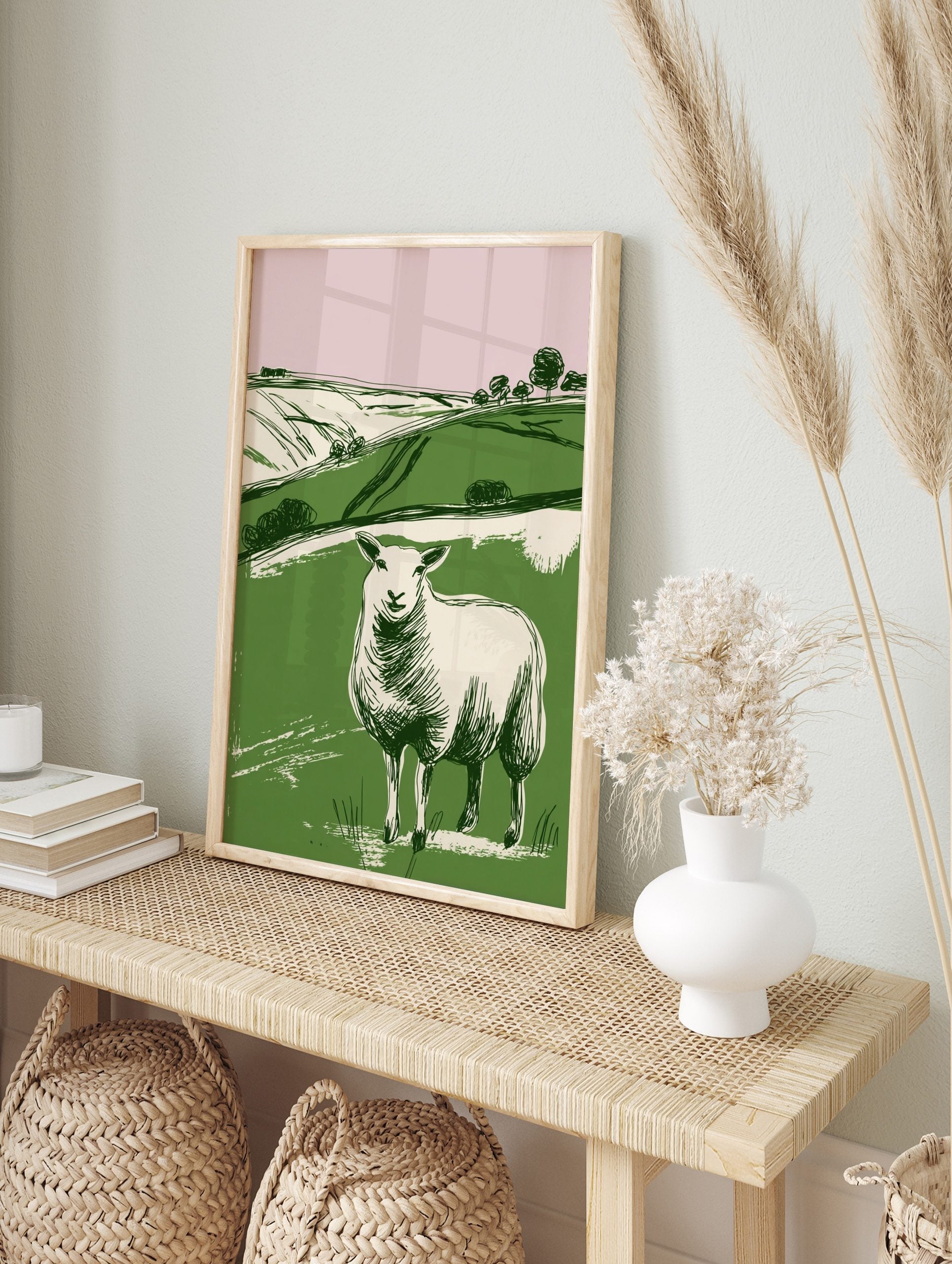 Illustrative print of a white sheep in a green field with rolling hills and pink sky, in a, in an alternate framed mockup