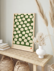 Illustrative pattern of white fluffy sheep on a green background with a red artist seal at, in an alternate framed mockup