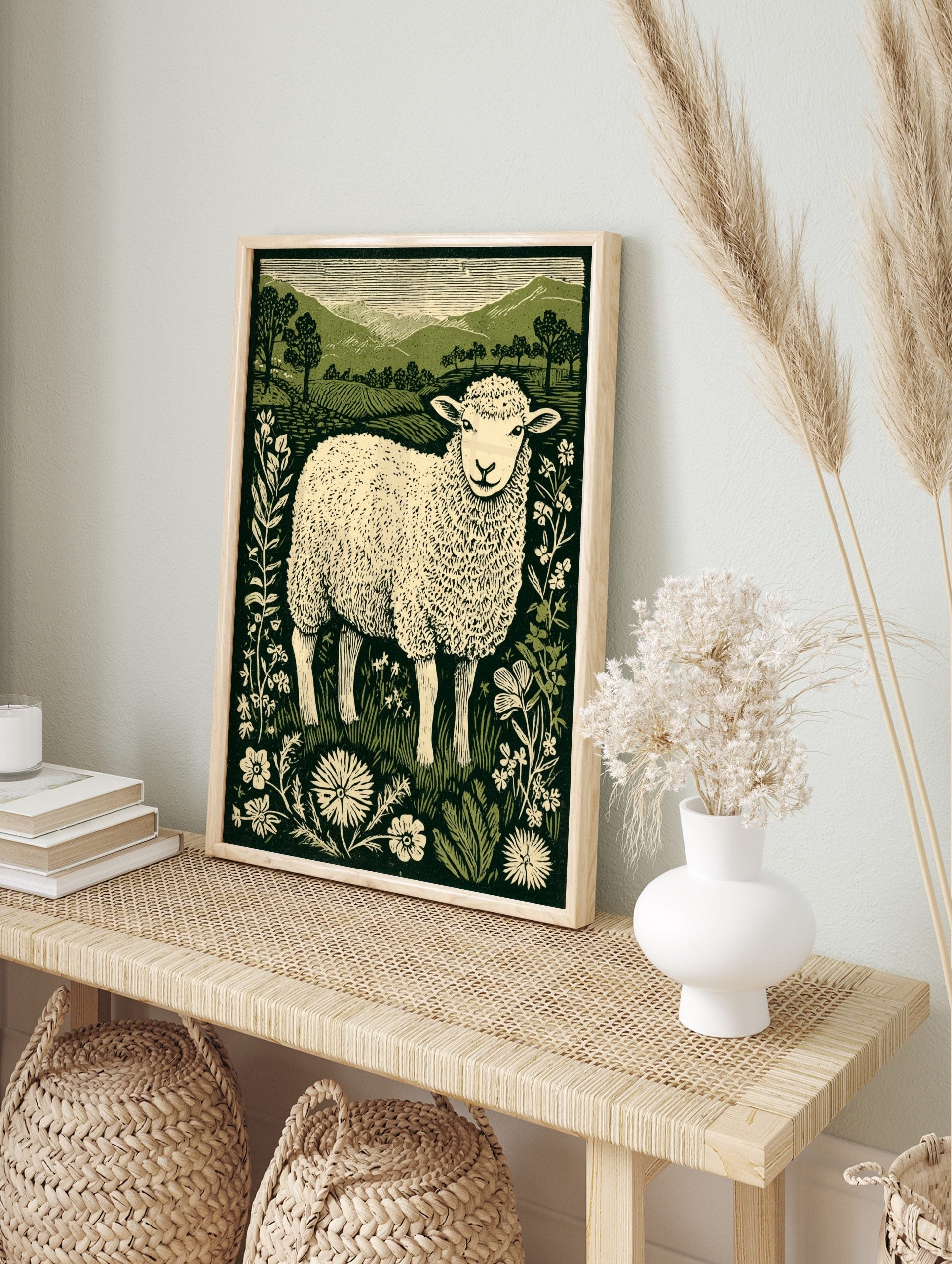 Linocut style print of a fluffy sheep in a field with wildflowers and green hills, green and, in an alternate framed mockup
