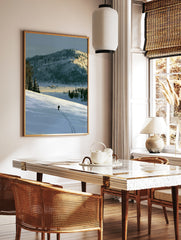 Illustrative art print of a lone skier on a vast snow-covered mountain landscape with blue and, in a styled room mockup