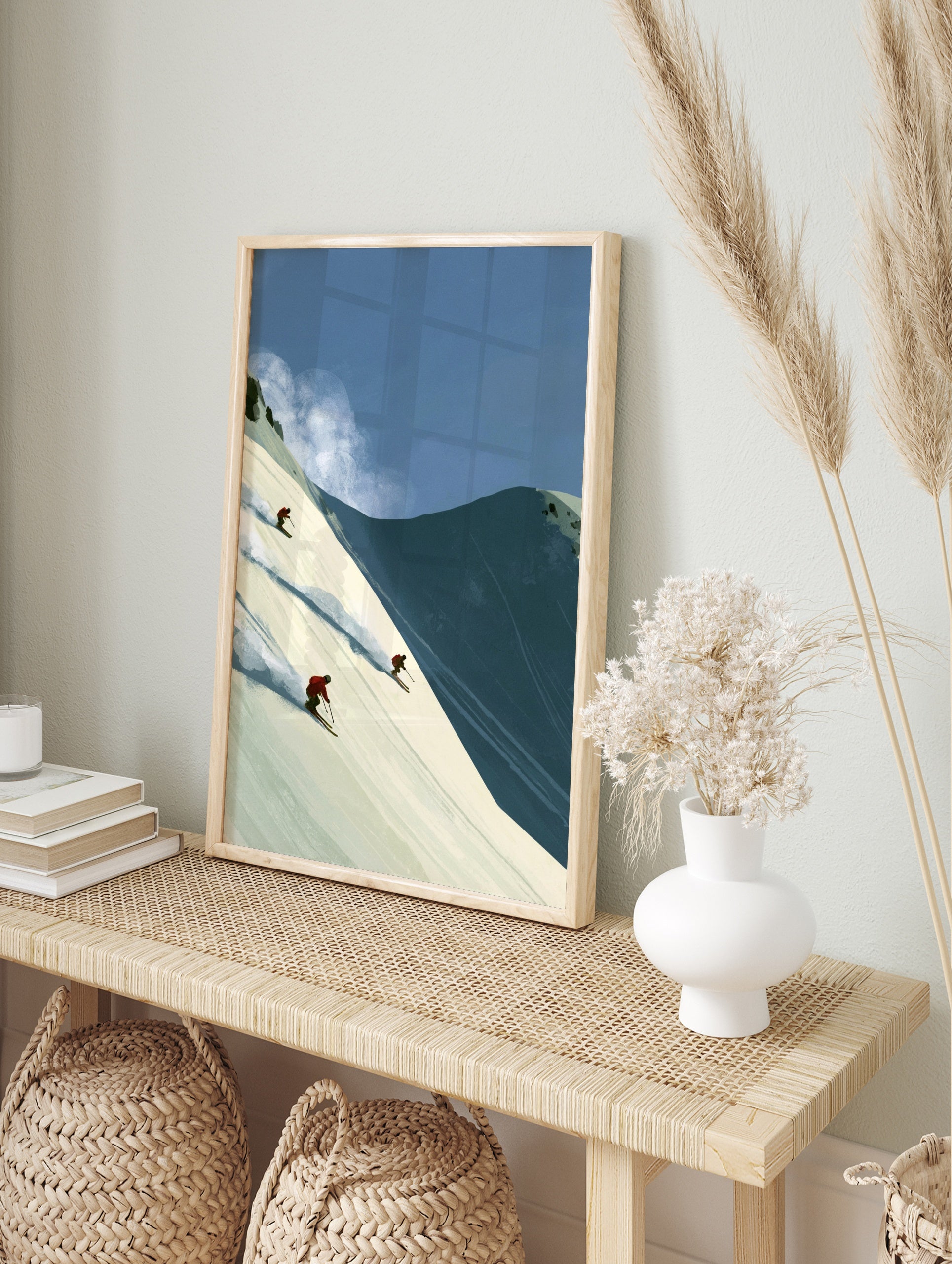 Illustrative wall art of three skiers in red jackets descending a steep snowy mountain slope, in an alternate framed mockup