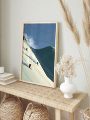 Illustrative wall art of three skiers in red jackets descending a steep snowy mountain slope, in an alternate framed mockup
