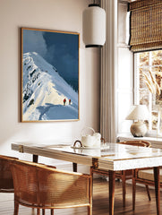 Illustrative mountain landscape art print featuring skiers in orange jackets on a snowy ridge under, in a styled room mockup