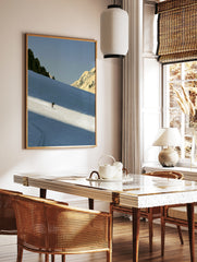 Minimalist skiing mountain wall art featuring a lone skier on a blue snowy slope with rocky peaks, in a styled room mockup