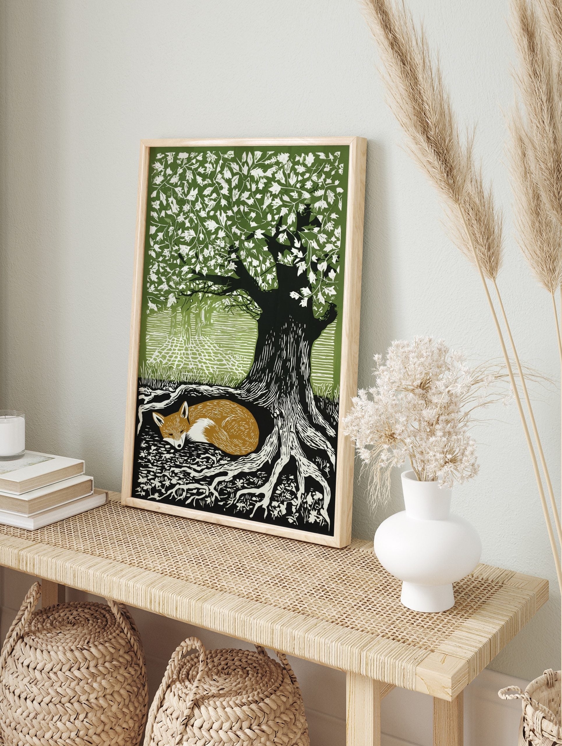 Woodcut style print of a sleeping russet fox curled at the base of a large tree with green, in an alternate framed mockup