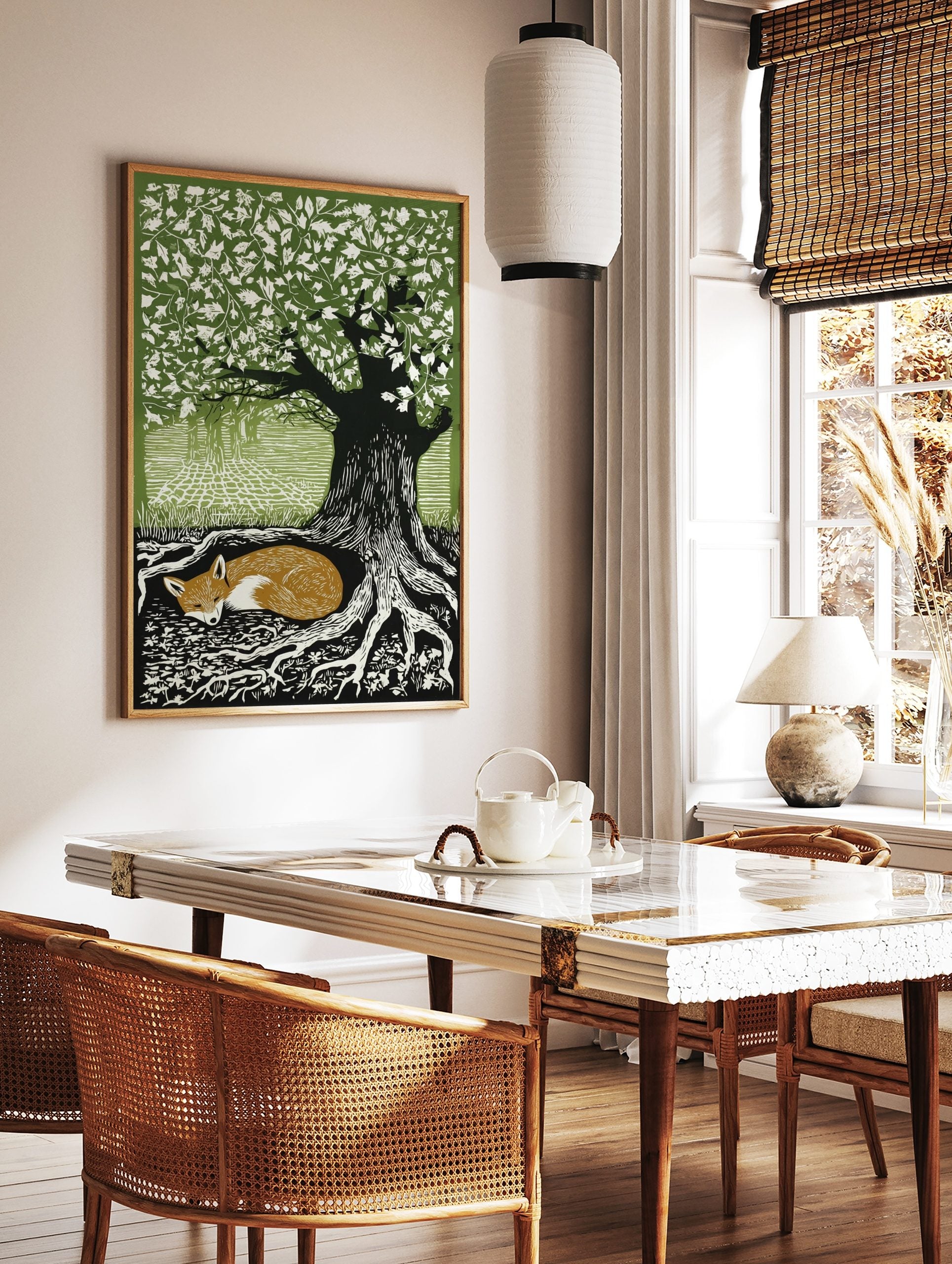 Woodcut style print of a sleeping russet fox curled at the base of a large tree with green leaves, in a styled room mockup