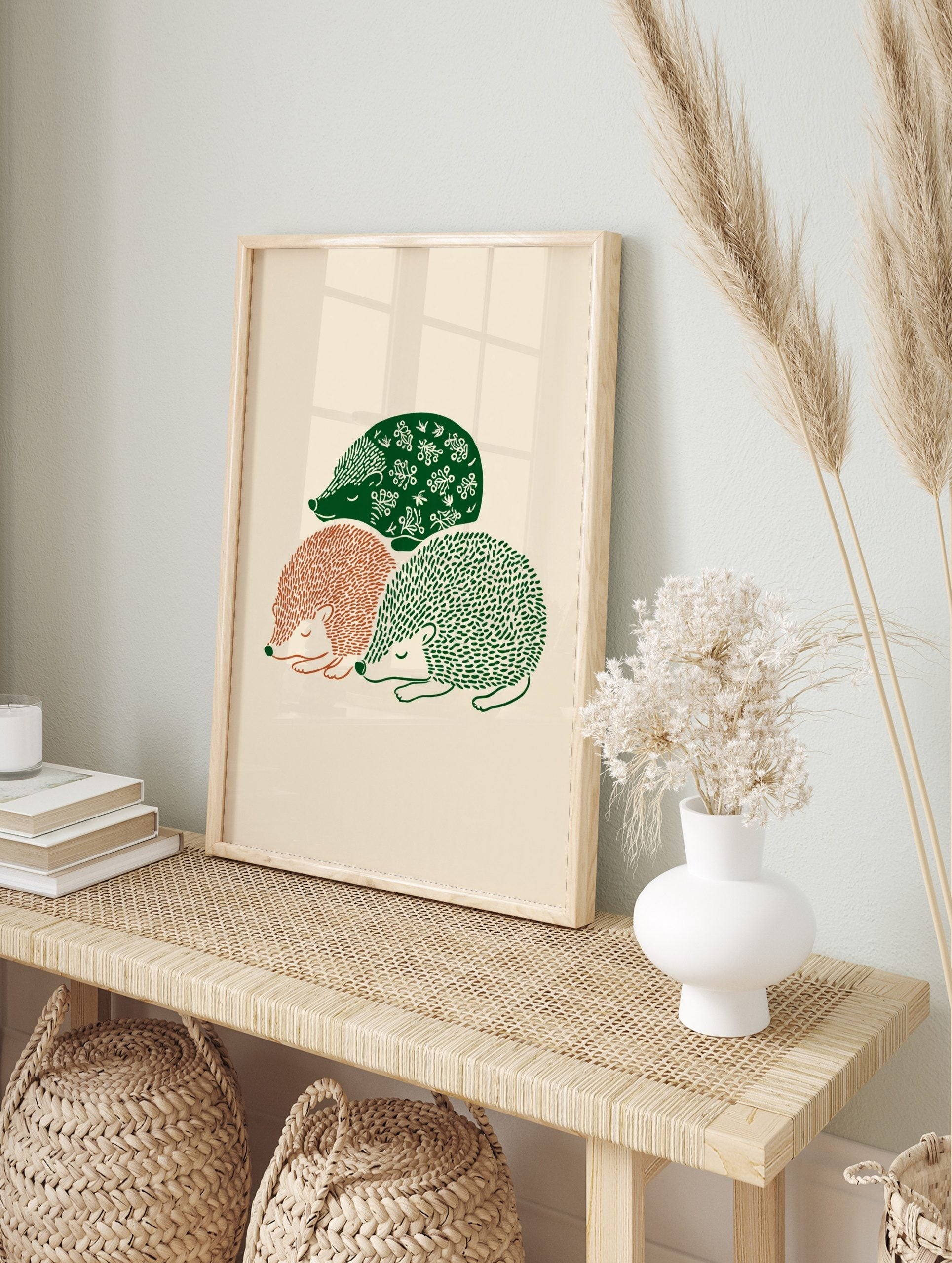 Three sleeping hedgehogs in green and terracotta folk art illustration on a beige background, in an alternate framed mockup