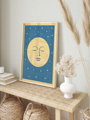 Stylised sleeping moon face illustration with closed eyes and gold stars on a blue, in an alternate framed mockup