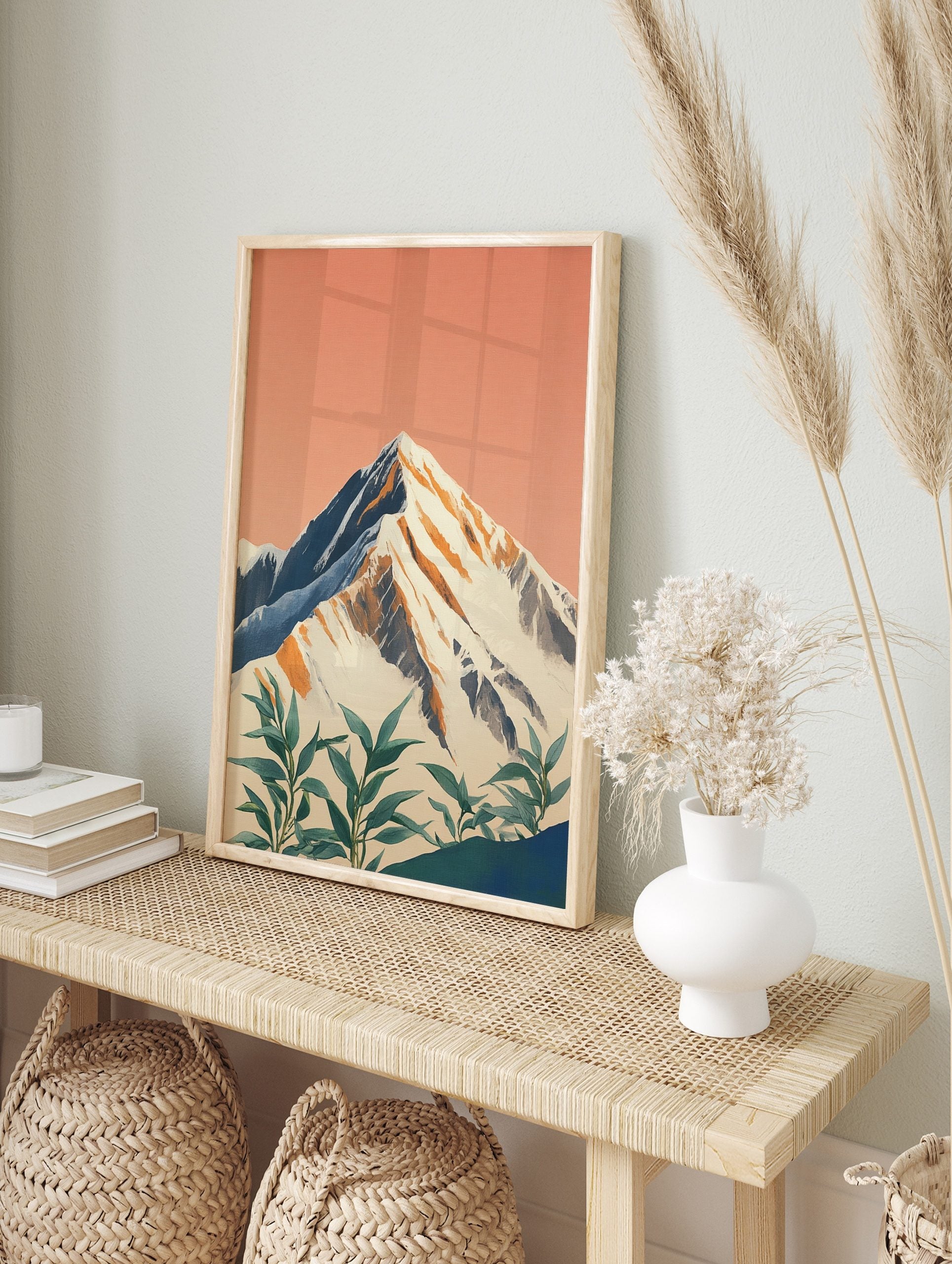 Illustrative snow-capped mountain print with peach sky and green foreground plants, in an alternate framed mockup