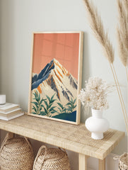 Illustrative snow-capped mountain print with peach sky and green foreground plants, in an alternate framed mockup