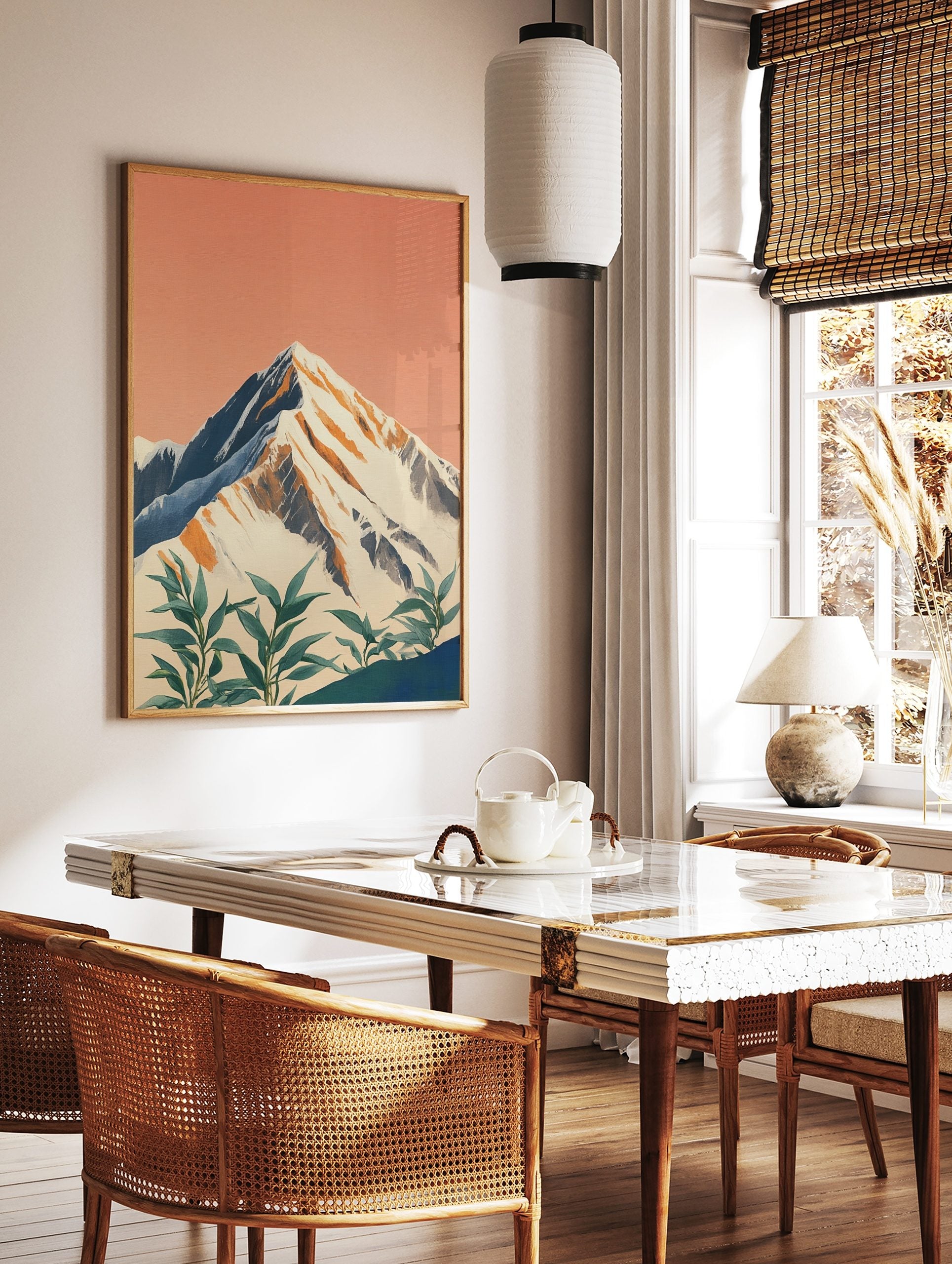 Illustrative snow-capped mountain print with peach sky and green foreground plants, in a styled room mockup
