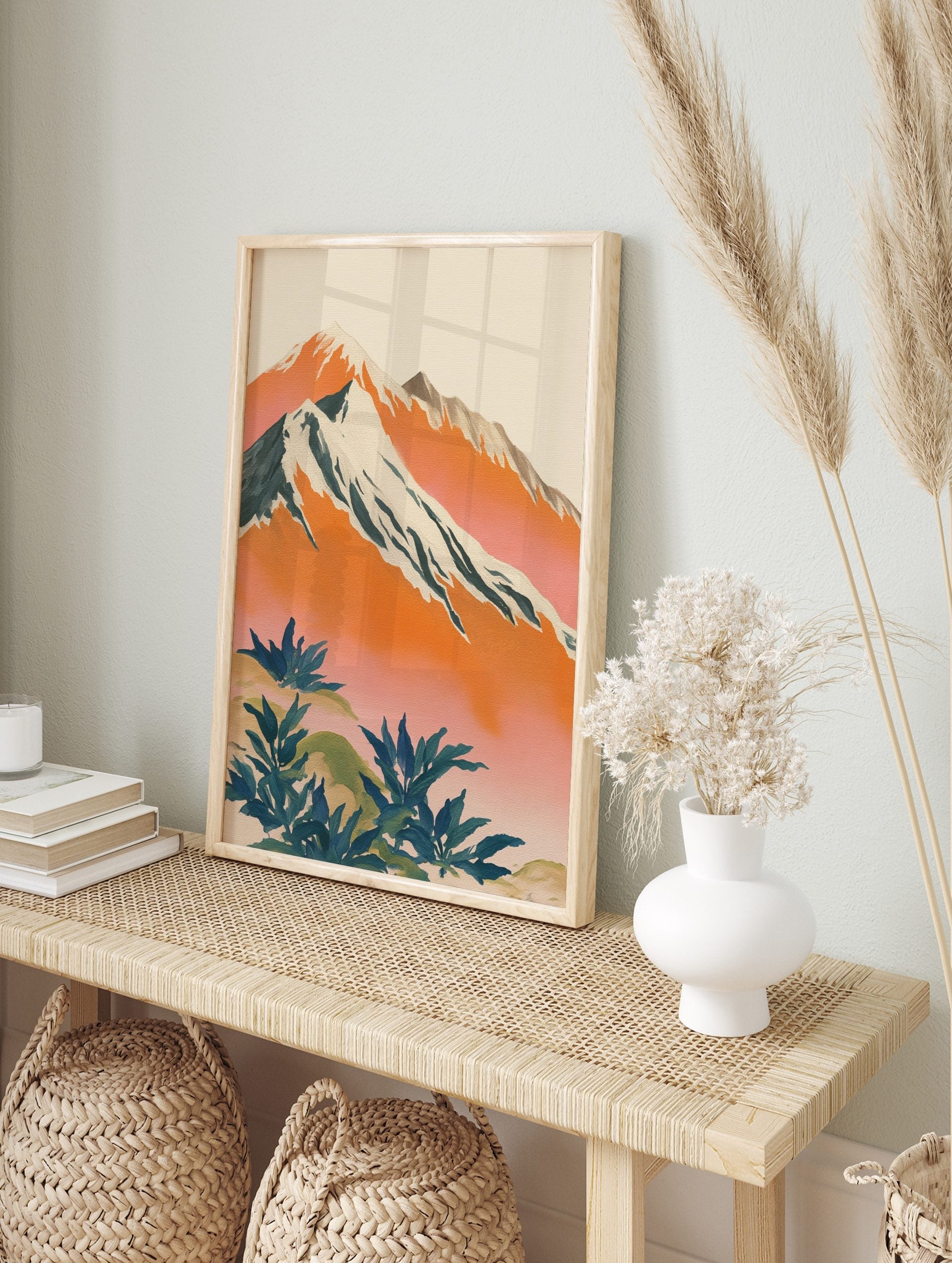 Illustrative mountain landscape art print with snow-capped peaks, orange and pink sky, and, in an alternate framed mockup