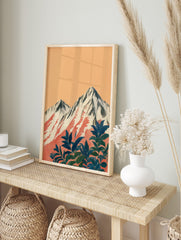Illustrative print of snow-capped mountains with red streaks and dark blue-green foliage, in an alternate framed mockup