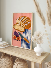 Illustrative art print of sliced sourdough bread, figs, and a striped tea towel on a pink, in an alternate framed mockup
