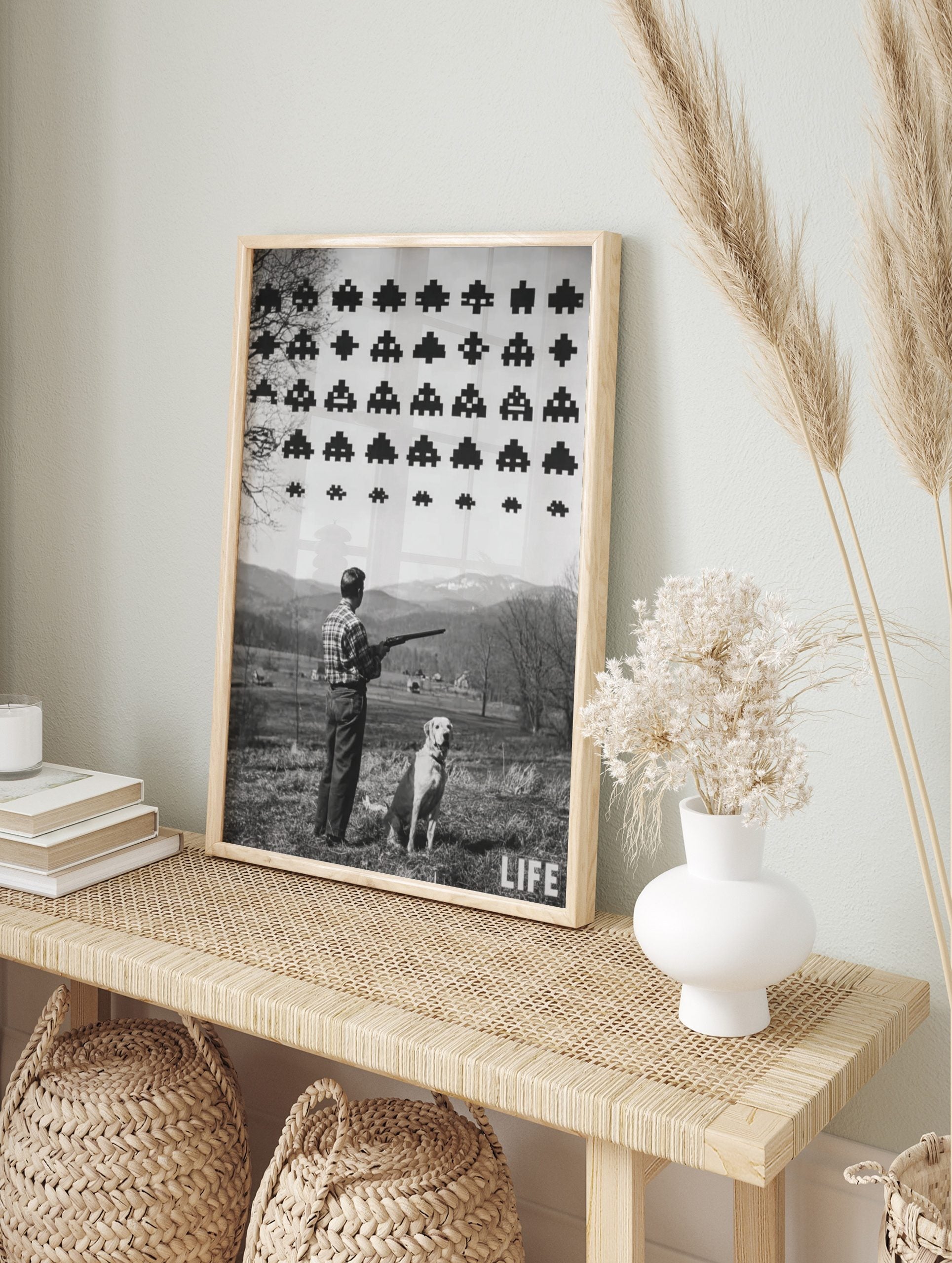 Monochrome print of man with shotgun and dog looking at pixelated Space Invaders in sky over, in an alternate framed mockup