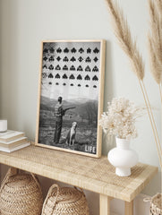 Monochrome print of man with shotgun and dog looking at pixelated Space Invaders in sky over, in an alternate framed mockup