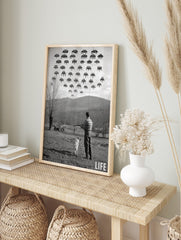 Monochrome print of a man and dog in a field looking up at pixelated Space Invaders in the, in an alternate framed mockup