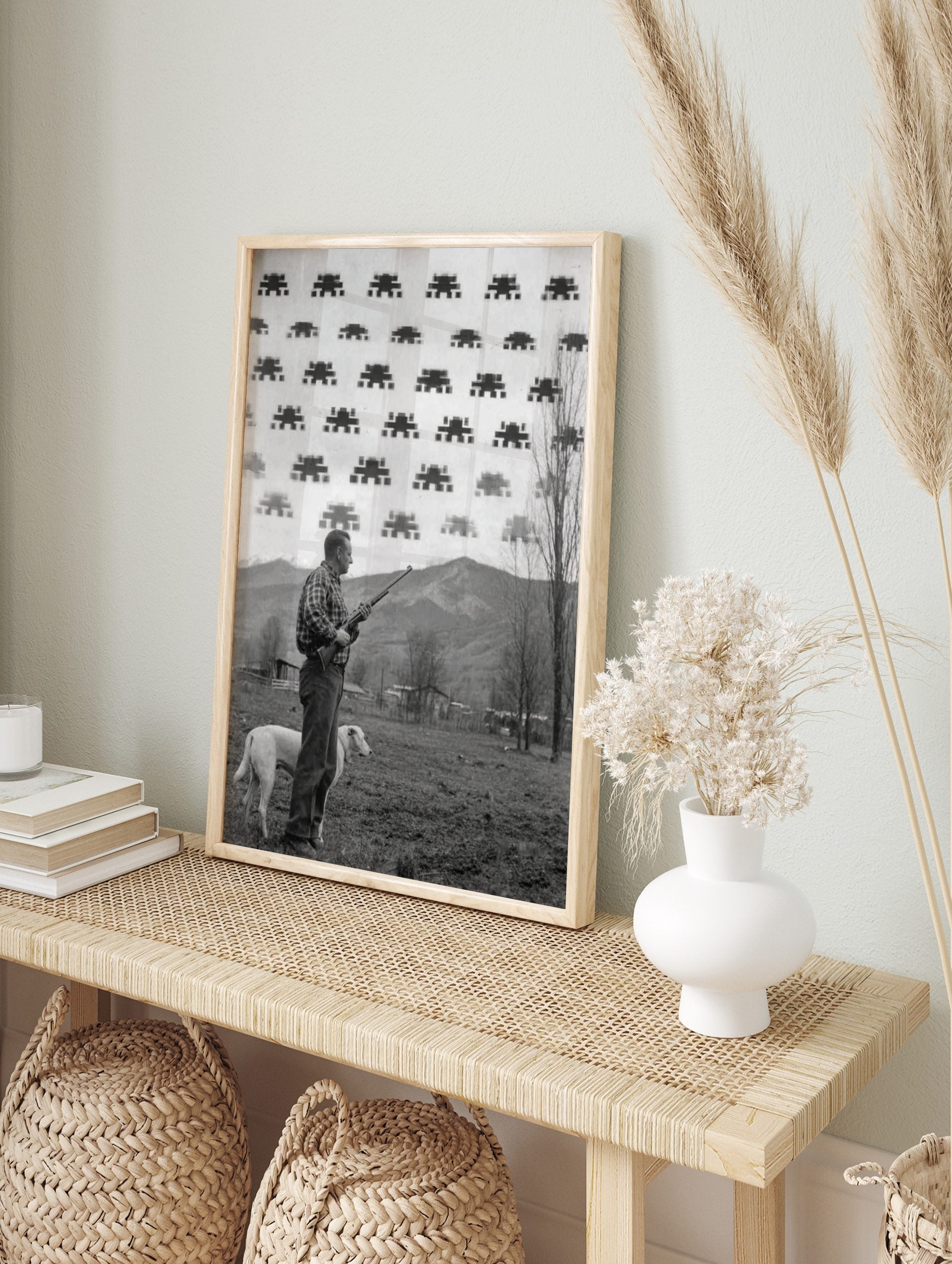 Monochrome print of a man with a rifle and dog looking at pixelated Space Invaders in the sky, in an alternate framed mockup
