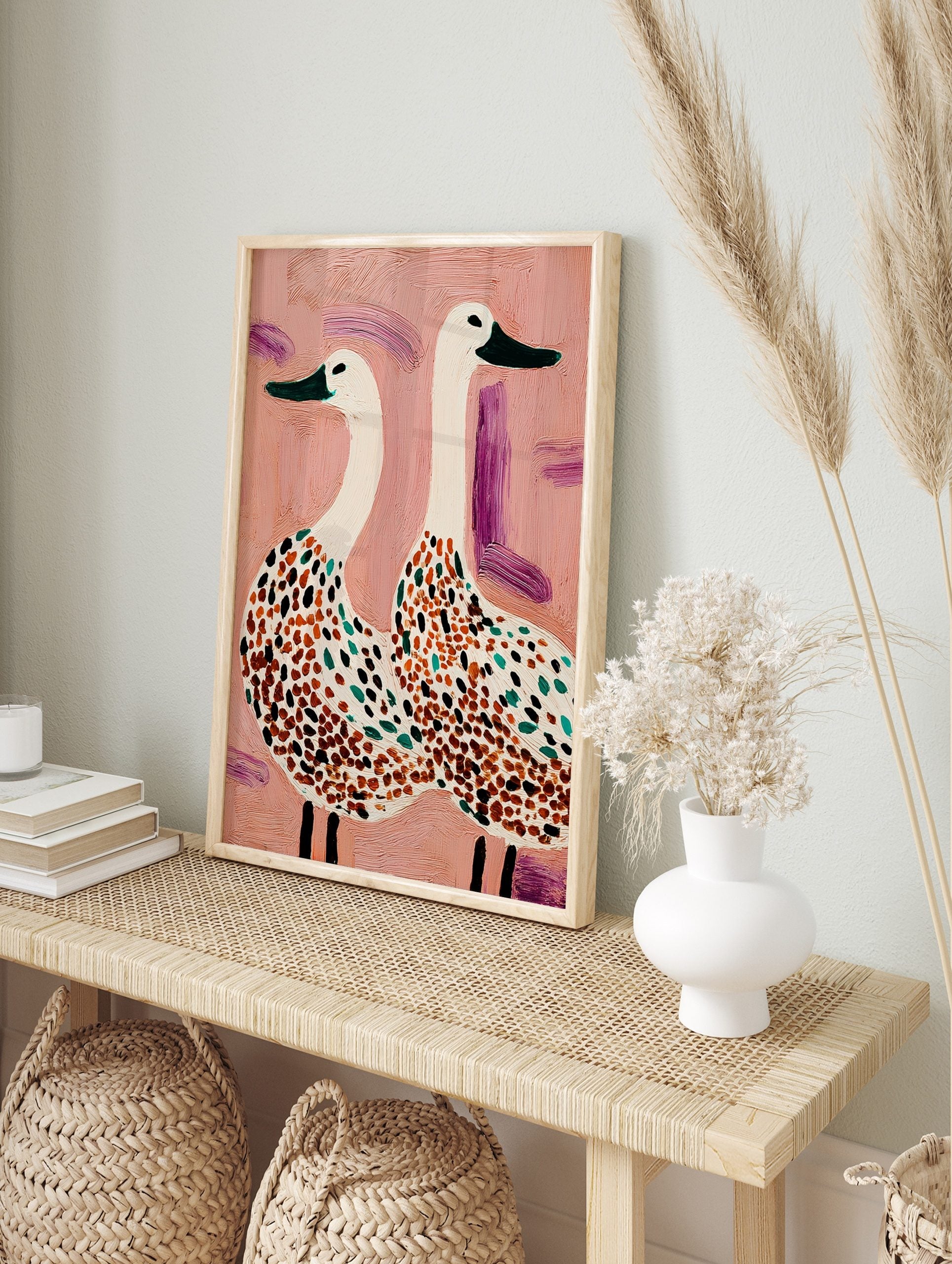 Illustrative wall art of two white spotted geese with green beaks on a textured pink, in an alternate framed mockup