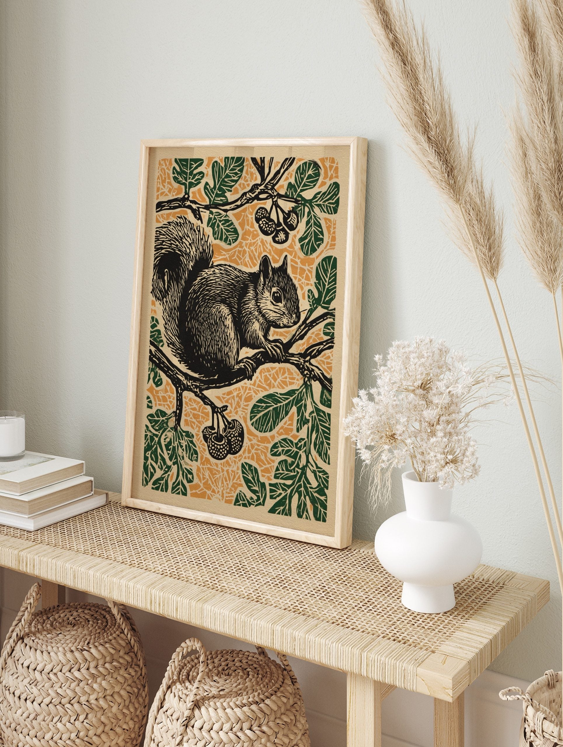 Linocut style print of a black squirrel on a tree branch with green leaves and berries, in an alternate framed mockup