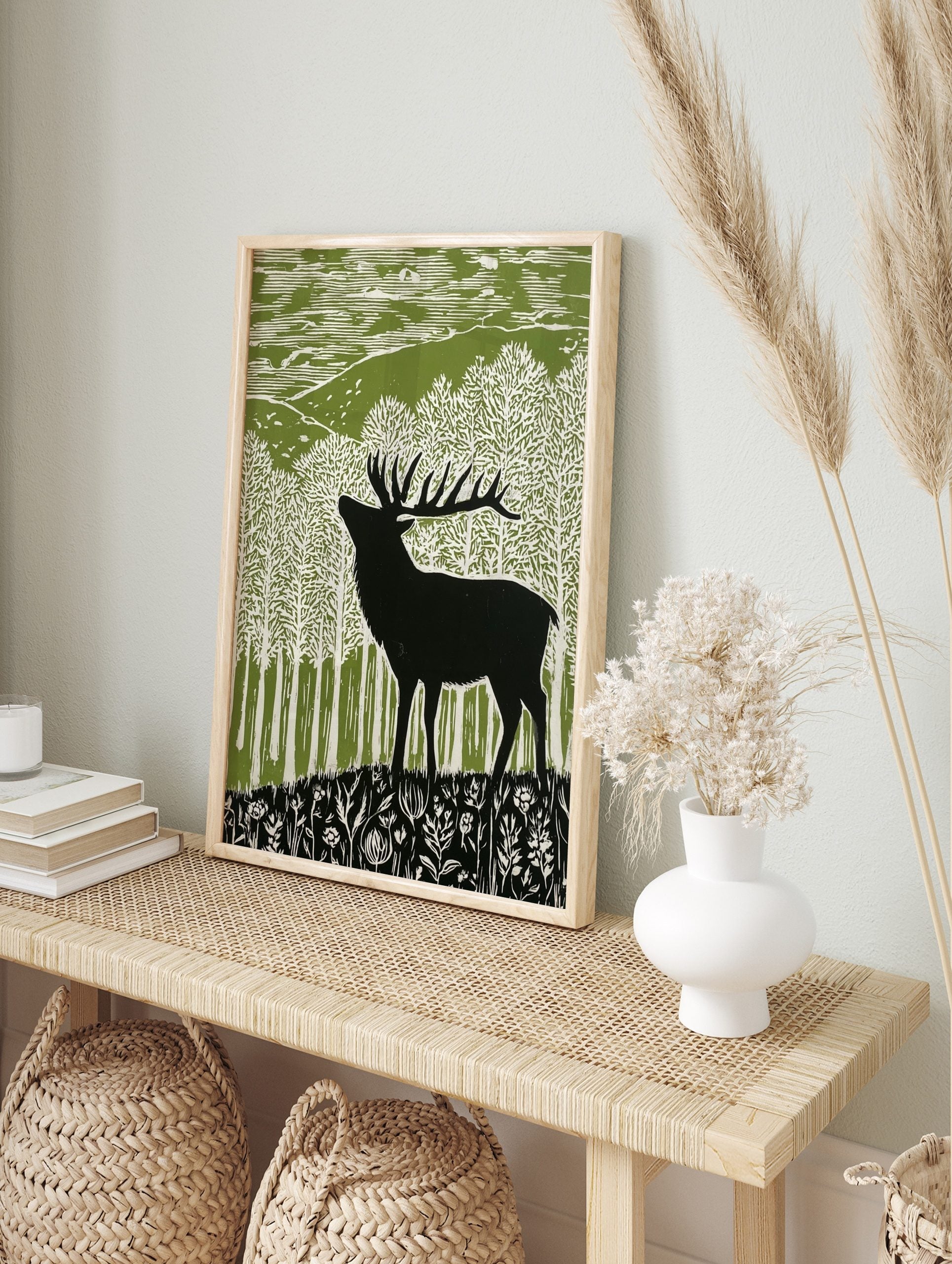 Lino cut style art print of a black stag deer in a green and white forest with hills and, in an alternate framed mockup