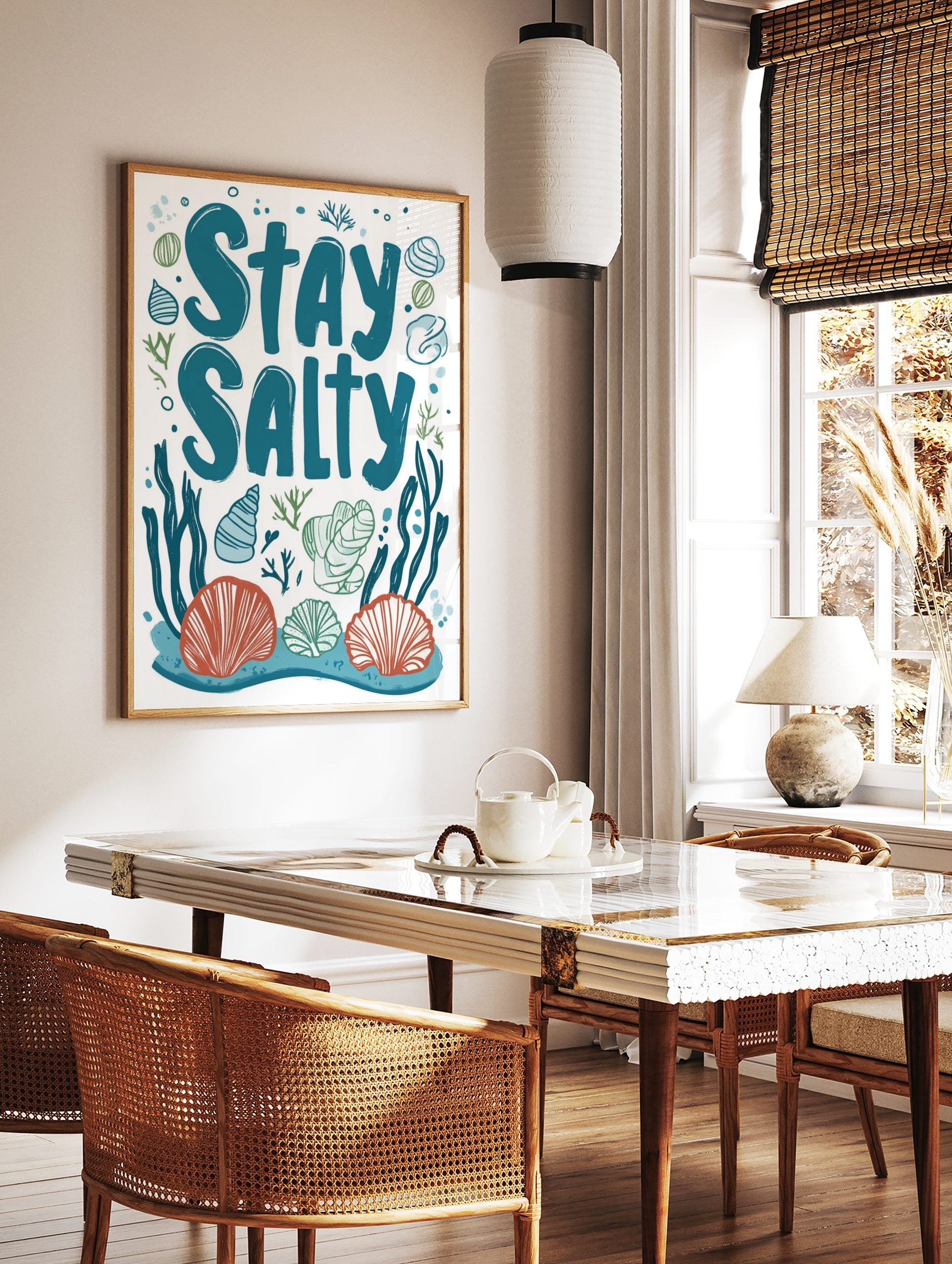 Stay Salty typography art print with teal text, orange and blue seashells, green seaweed on white, in a styled room mockup