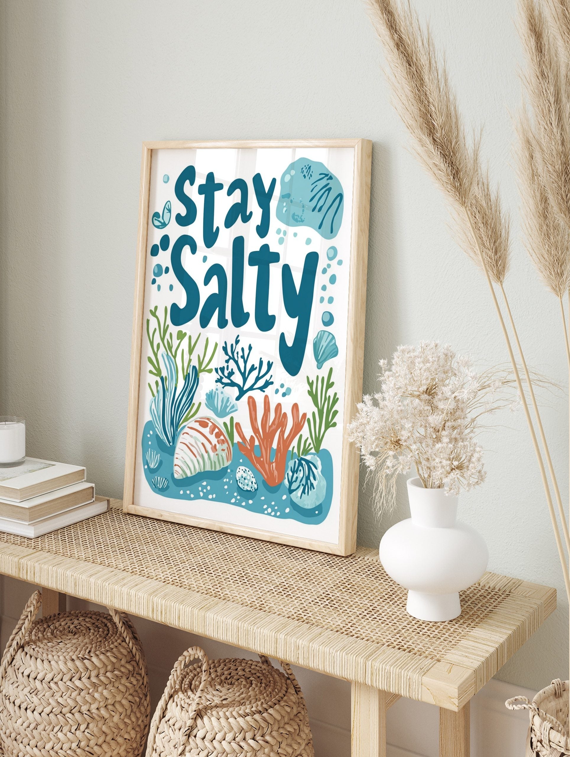 Stay Salty typography print with blue text, orange coral, green seaweed, and seashells on a, in an alternate framed mockup