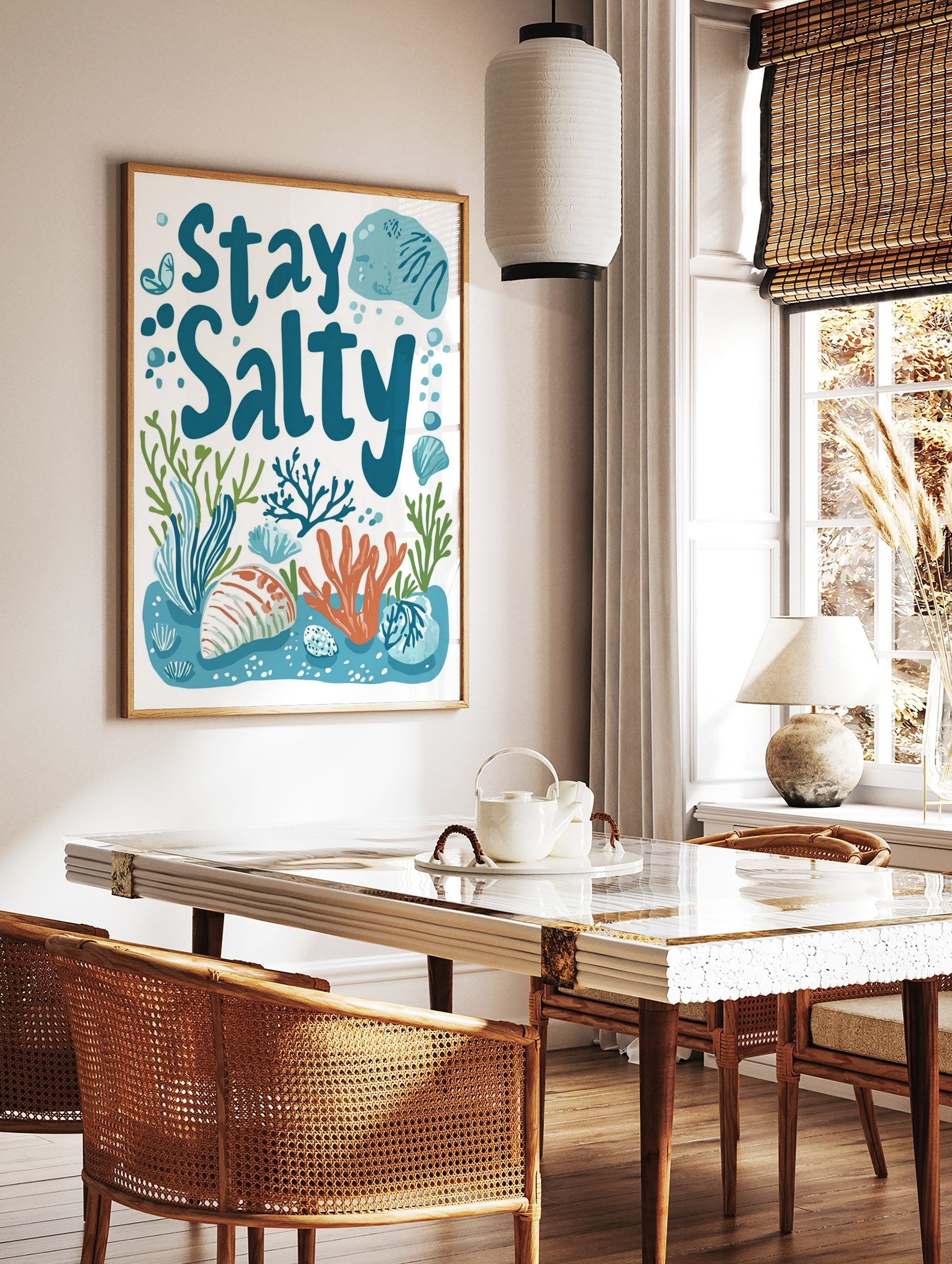 Stay Salty typography print with blue text, orange coral, green seaweed, and seashells on a white, in a styled room mockup