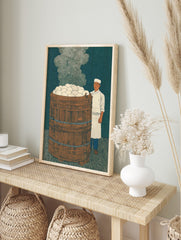 Illustrative print of a chef next to a large wooden steamer barrel overflowing with white, in an alternate framed mockup