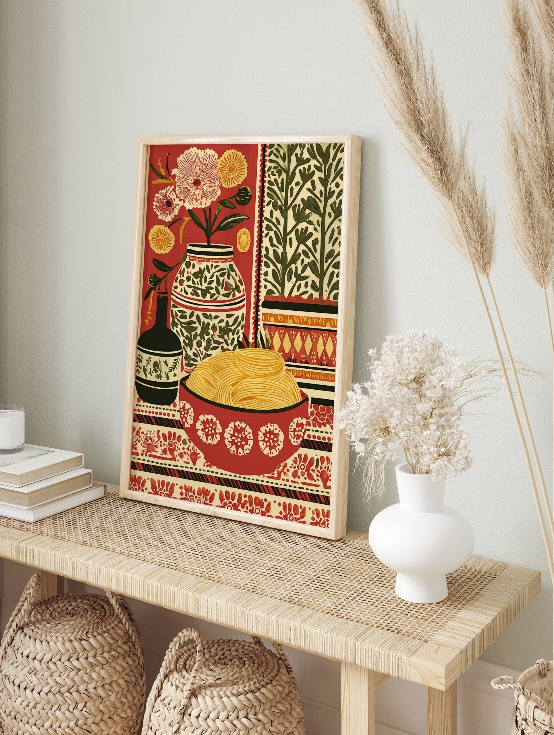Still life folk art print with a bowl of pasta, flowers in vases, and patterned textiles on a, in an alternate framed mockup